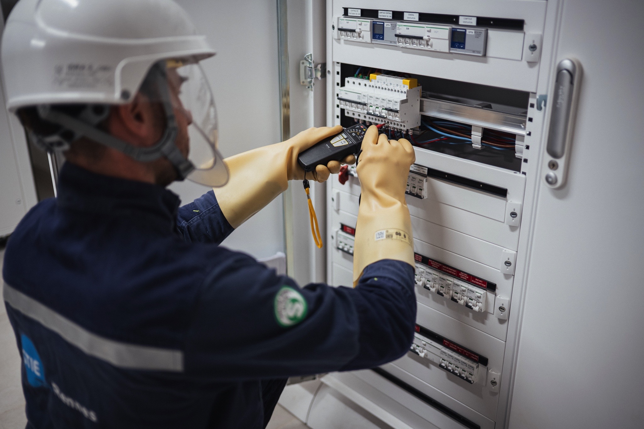 Technicien équipé d’EPI réalisant des mesures et vérifications sur un tableau électrique basse tension à l’aide d’un appareil de contrôle.
