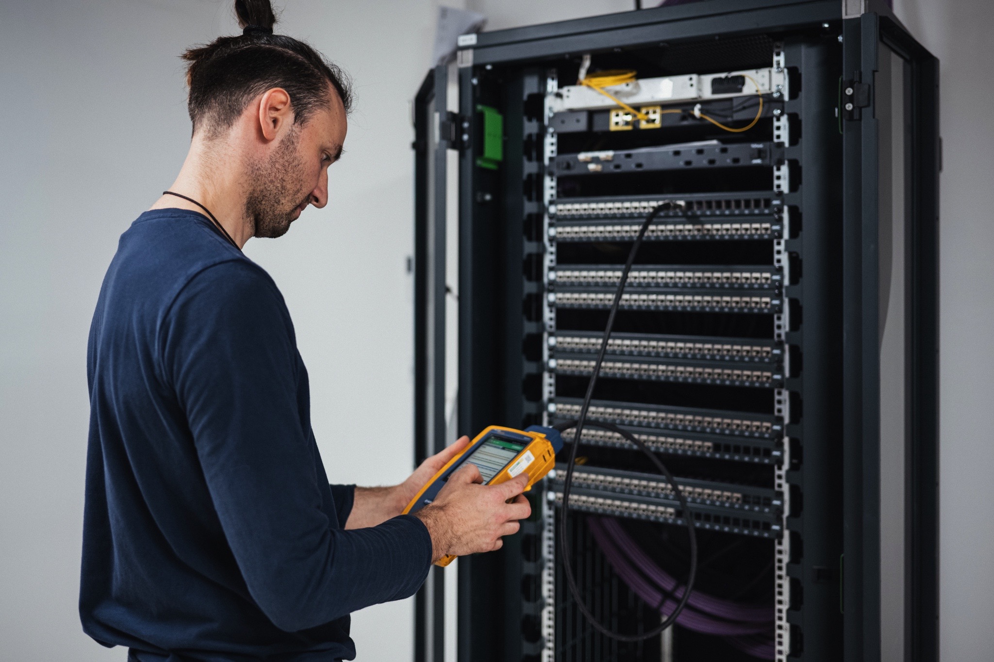 Technicien réalisant des tests et mesures sur une baie de brassage afin de vérifier les performances du réseau informatique.