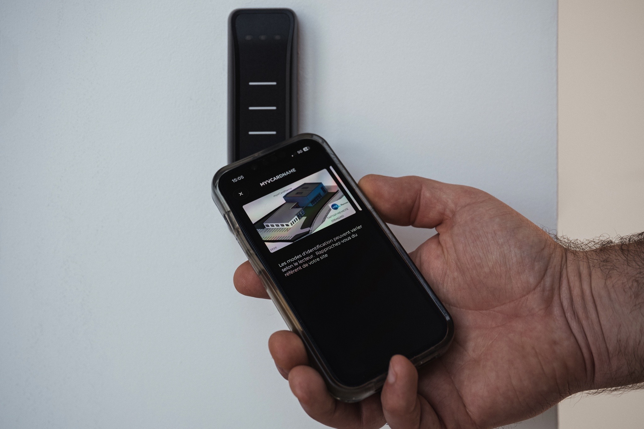 Utilisateur utilisant une application mobile pour accéder à un système de contrôle d'accès connecté via un lecteur mural.