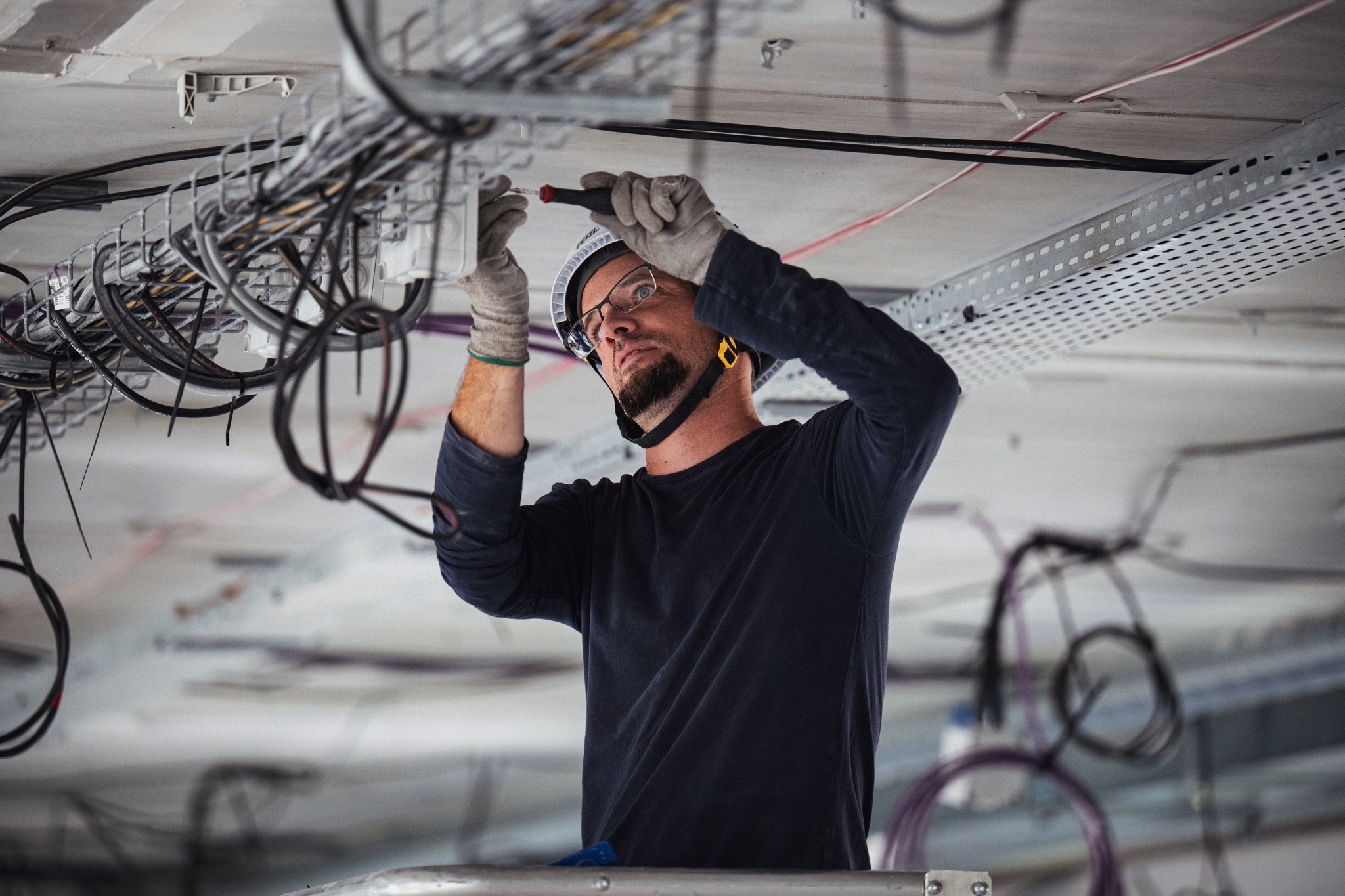 Technicien réalisant le raccordement et l’organisation de câbles électriques et de communication sur un chemin de câbles en plafond technique.