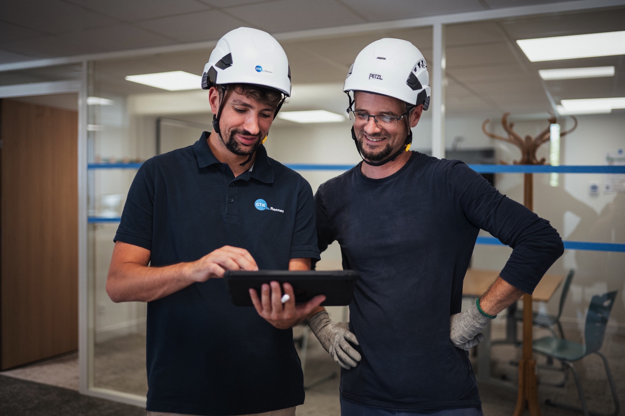 Deux techniciens consultent une tablette numérique afin de suivre l’avancement d’une intervention technique dans un bâtiment tertiaire.